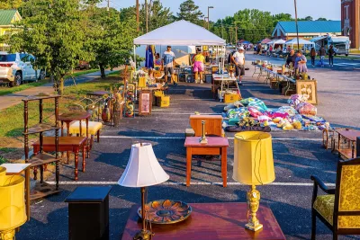 Tables full of second hand stuff set up in parking area with canopies over them and vintage lamps on tables in foreground.