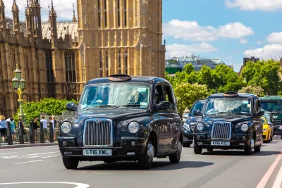 Line of traditional London black cabs passing in front of Westminster Abbey.