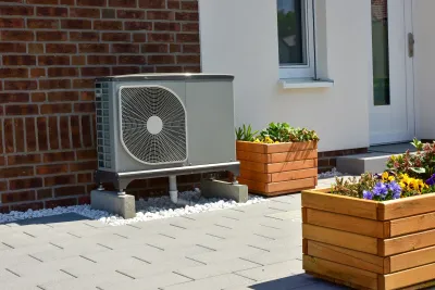 Heat pump installed next to brick wall on  residential building next to brown wood planter boxes.
