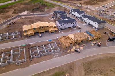 Aerial of wood-framed homes under construction in cleared dirt lots.