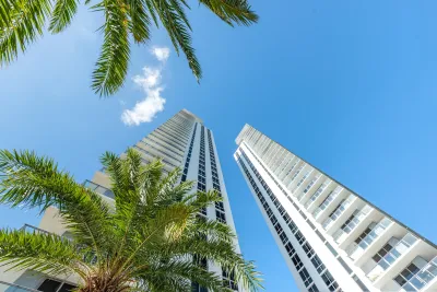 Looking up at modern high-rise buildings with palm trees in foreground against bright blue sky in Miami, Florida.