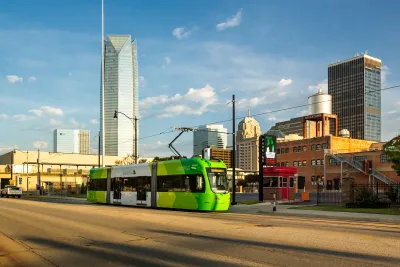 Green Oklahoma City streetcar with downtown skyline in background.