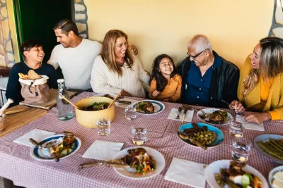 Happy family sitting at table with checkered red and white tablecloth and multiple plates and bowls of food.