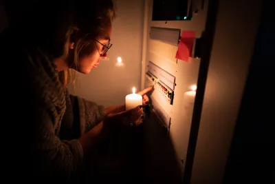Person holding up candle to power panel in the dark.