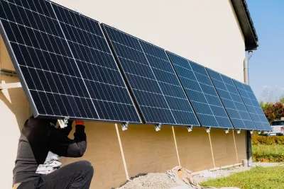 A person installing solar panels on a wall. The panels are tilted slightly, the head of the person is hidden under one of them.