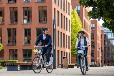 Young man and woman on bike share bikes riding in city.