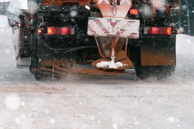 Close-up on back of yellow truck putting down road salt on icy road.