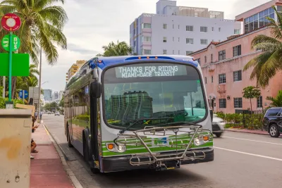 A Miami-Dade green bus, surrounded by brick buildings.