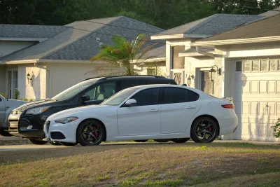 Black SUV and white sedan parked in driveway in front of house.