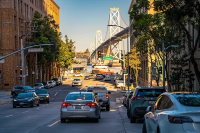 Cars on a small street with view of bridge over bay in San Francisco, California.