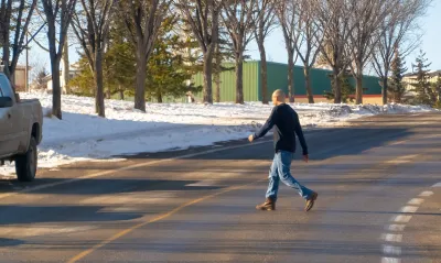 Man in jeans and black shirt crossing street mid-block in winter.