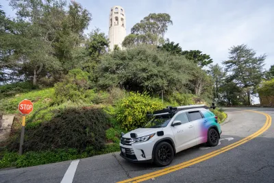 A white Zoox self-driving car going down windy hill in San Francisco next to Coit Tower.