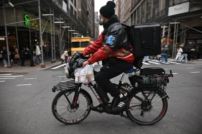 Delivery worker carrying take-out food wearing a black backpack on black bike in New York City.
