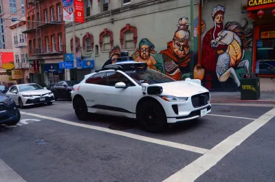 White Waymo Jaguar car on street with colorful mural in background in San Francisco, California.