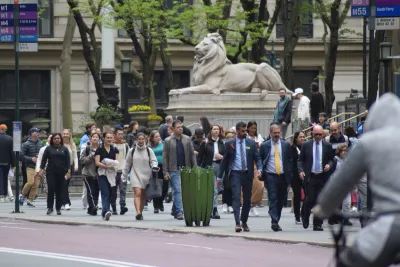 Busy sidewalk in New York City in front of NY Public Library with large stone lion statue.