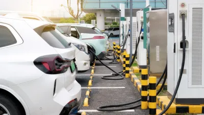 Row of various white cars plugged into EV charging stations outdoors.