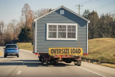 A manufactured house on the back of a truck driving down a road.