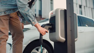 Close-up of person in denim jacket plugging in eledtric car to curbside charger.