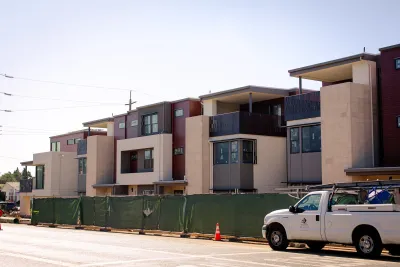 Two-story apartment or condo building under construction behind green construction fence in Cupertino, California.