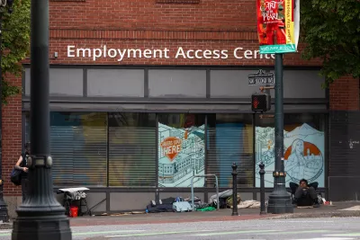 Unhoused people camped in front of brick building with "Employment Access Center" sign in Portland, Oregon.