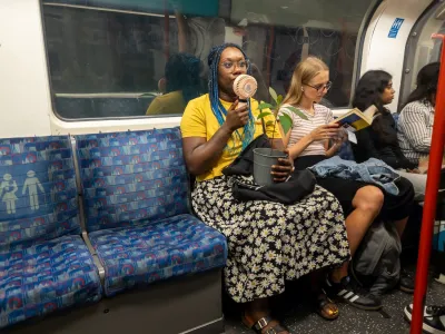Woman sitting in subway car holds up small portable fan to cool herself.