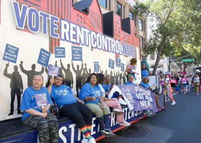 Float supporting rent control with "Vote rent control now" banner behind several sitting people drives through Oakland Pride parade in 2024.