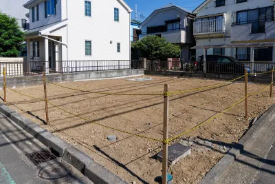 Vacant dirt lot surrounded by yellow and black rope among two-story houses.