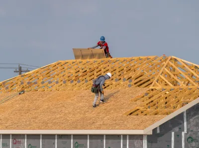 Two construction workers on roof of wood-framed house.