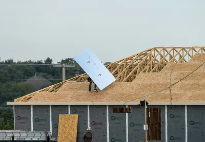 Two workers putting reflective insulation panels into roof of wood-framed house under construction.