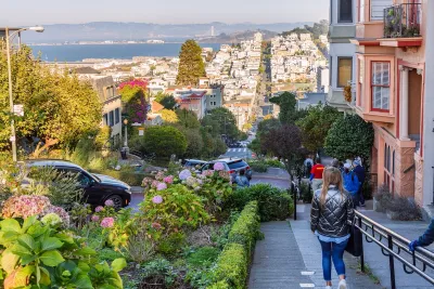 View from top of hill in San Francisco with people walking down sidewalk next to historic Victorian homes.
