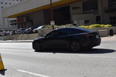 Black Tesla car on street in Houston, Texas next to building with red sign for AMC movie theater.