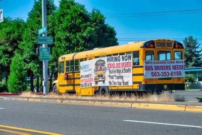 Yellow school bus parked on roadside with signs advertising bus driver jobs.