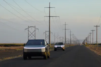Two silver Cybertrucks driving down rural road with fog,