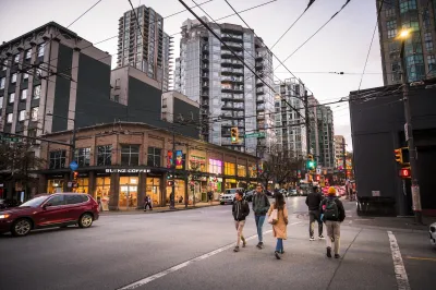 People in a crosswalk in downtown Vancouver, BC with tall glass apartment towers in background and streetcar cables criss-crossing above the street.