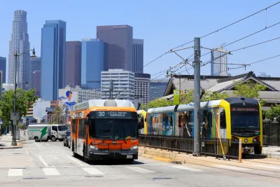 Orange bus and yellow light rail train next to each other on street with downtown Los Angeles visible in background.