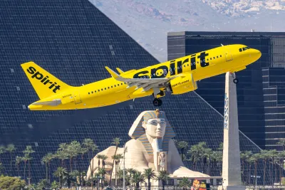 Yellow Spirit Airlines plane taking off in Las Vegas with replica pyramid and Sphynx in background.