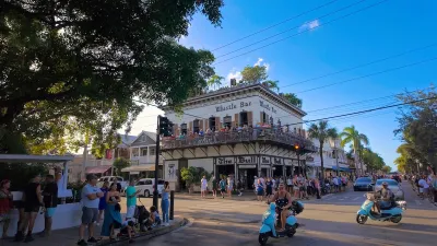 People on mopeds turn a corner in Key West, Florida. A two-story bar is in the background.