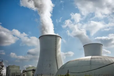 Two large cooling towers with white steam rising out at nuclear power plant.