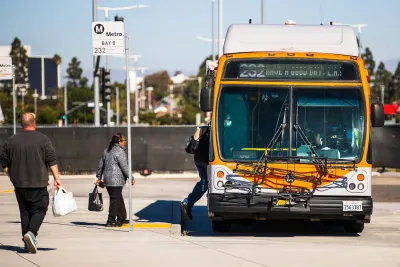 Three people boarding an orange Los Angeles Metro bus at an unsheltered stop on a sunny day.