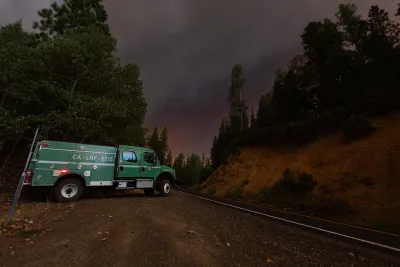 Green wildland firefighting truck parked on road with wildfire sky in the distance.