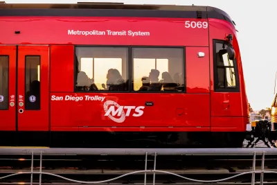 Red San Diego light rail train with people visible inside.