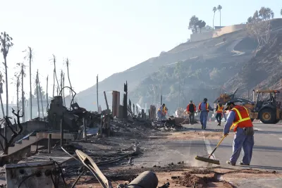 People in orange safety vests sweeping and cleaning debris in Eaton Fire burn area in Malibu.