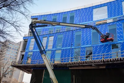 Construction crane in front of apartment building under construction with blue unfinished facade in Philadelphia.