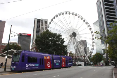 View of giant Ferris Wheel in downtown Atlanta, Georgia in Centennial Olympic Park. Purple public tram (light rail vehicle, popular streetcar) stops in front.