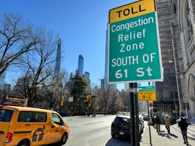 Green congestion pricing sign on side of street in New York City with yellow van cab visible on street.