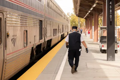 An Amtrak conductor walks parallel to an Amtrak train. 