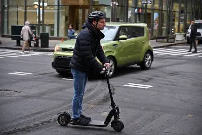 A man wearing a helmet rides an e-scooter on a street in Manhattan.