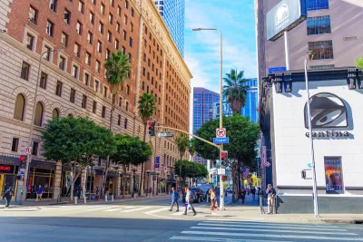 A downtown area in Los Angeles, with a Taco Bell visible. People wait to cross the street towards a tall apartment building.