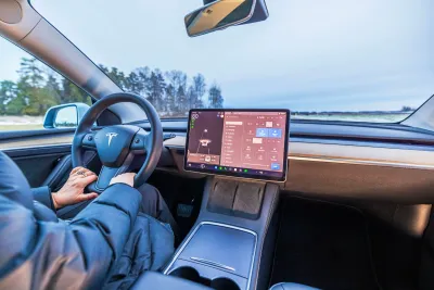 Interior of Tesla car with person's hands on steering wheel and large screen in middle.