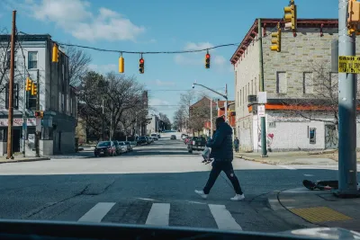 A person crossing a street under hanging traffic lights in Maryland.